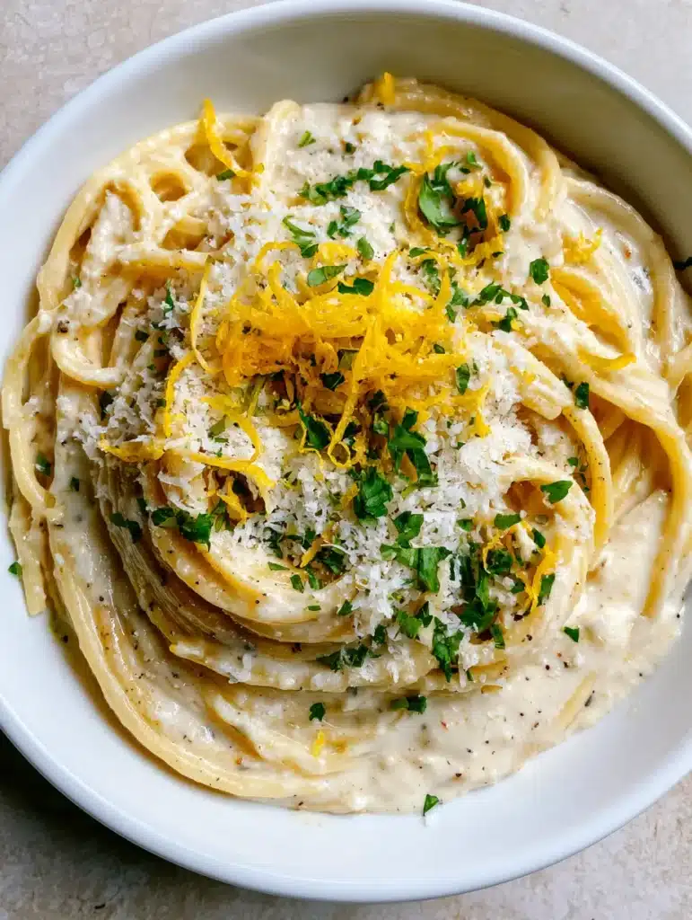 Lemon Ricotta Spaghetti scattered with bright green parsley and white Parmesan cheese on a stone countertop.