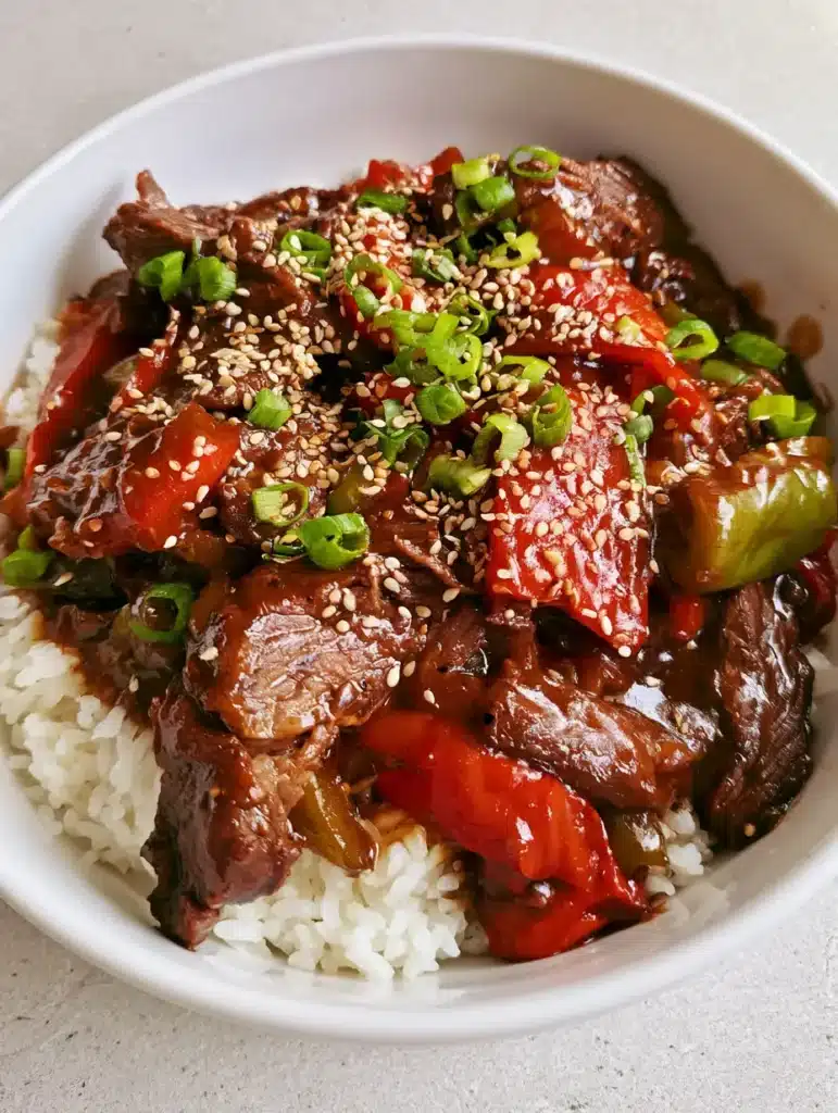 Slow Cooker Pepper Steak with Tender Flank Steak and Glossy Gravy 1 Vibrant red and green bell peppers mixed with seared beef in a white bowl of Slow Cooker Pepper Steak.